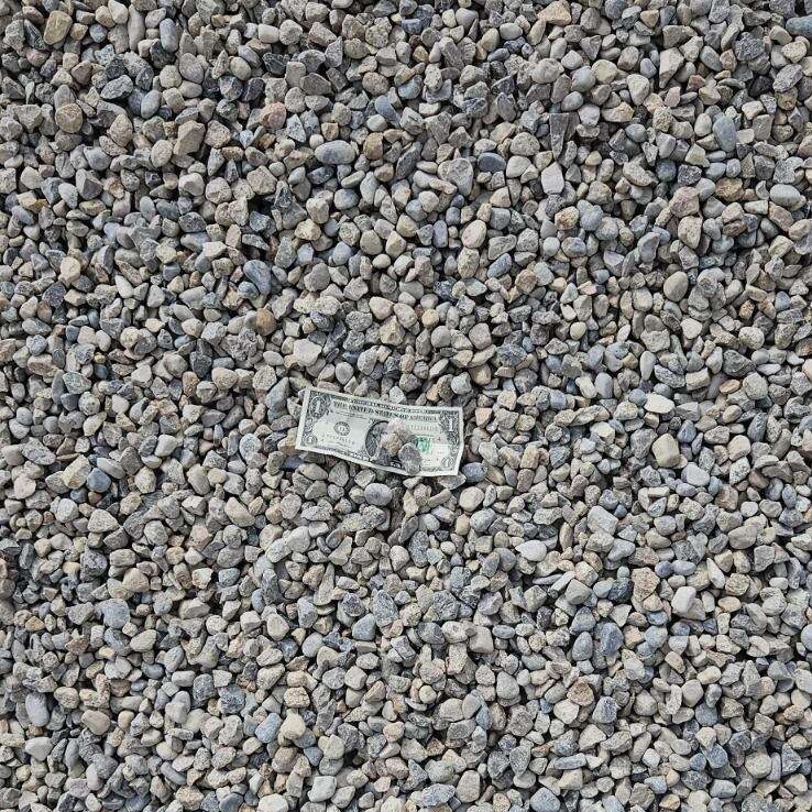 Darby Pit, Gravel & Trucking - We specialize in supplying top-quality materials including dirt, sand, gravel, and crushed stone to meet all your construction and landscaping needs. Whether you're working on excavation projects, constructing roads or driveways, laying foundations for new homes, or enhancing your outdoor spaces with beautiful paths and landscaping features, we have you covered. Our comprehensive trucking services ensure timely delivery of these essential materials to builders and homeowners alike. In the midst of a ground covered with small gray 3/4” chips lies a $5 bill. The tip of a work boot is visible in the bottom left corner—perhaps from someone ready to get started on their next big project with our reliable materials and services.