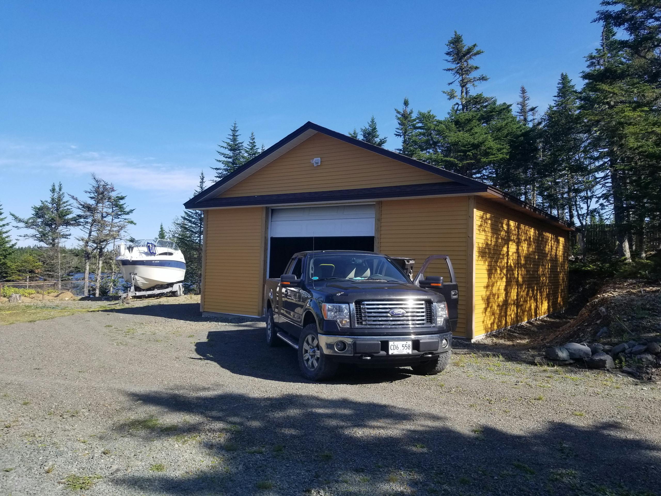 A parked truck in front of a yellow garage with a boat nearby in a rural setting.