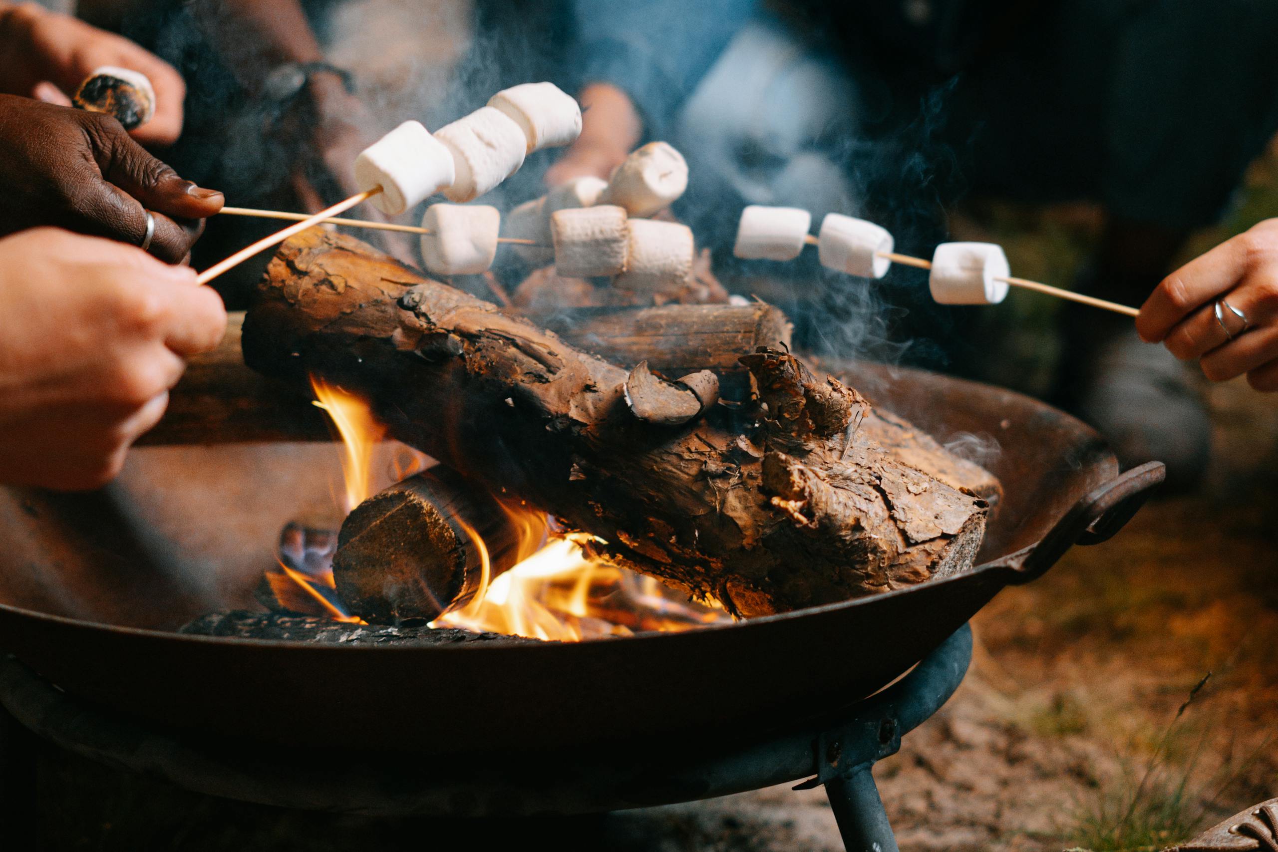 Hands roasting marshmallows over a campfire, creating a cozy outdoor snack moment.